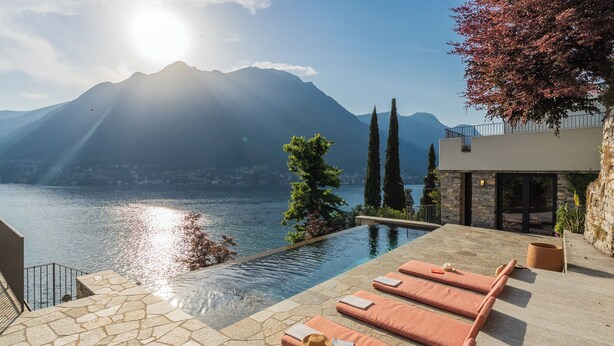 An infinity pool with lounge chairs, a stone pathway, and a mountain view. - Villa Madonnina (Pognana Lario)