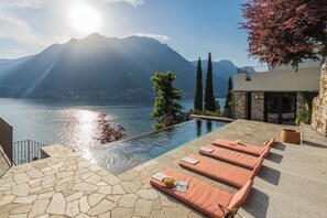 An infinity pool with lounge chairs, a stone pathway, and a mountain view. - Villa Madonnina (Pognana Lario)