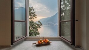 A window with a view of a lake and mountains, a wooden tray with fruits, and a clear sky. - Villa Madonnina (Pognana Lario)