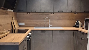 A modern kitchen with dark cabinets, a wooden countertop, a stainless steel sink, and a built-in oven. - Beautifully renovated family home (Saint-Romain)