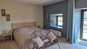 A bedroom with a bed, a wicker chair, a bedside table, a window with a view, and wall-mounted artwork. - Beautifully renovated family home (Saint-Romain)