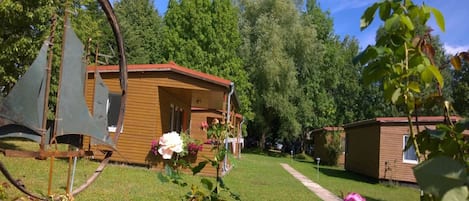 A wooden cabin with a porch, surrounded by a well-maintained lawn and trees.