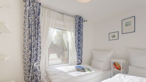 Ein Schlafzimmer mit zwei Betten, einem Nachttisch mit Lampe und einem Fenster mit Vorhängen.