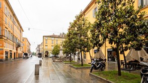 Eine nasse Stadtstraße mit Gebäuden, Bäumen und abgestellten Rollern.