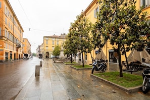 A wet city street with buildings, trees, and parked scooters. - A practical 40 square meters studio apartment, perfect for three people, located on the fourth floor of a building without an elevator.The property is located in a centrally located area (limited traffic zone) of Modena, allowing our guests to explore th (Modena)