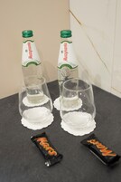 Dos botellas de cerveza Muszynka, dos vasos y dos barras de chocolate Mars sobre una superficie oscura.