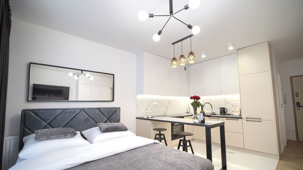 Una habitación de hotel moderna con cama, espejo, zona de cocina y mesa de comedor.