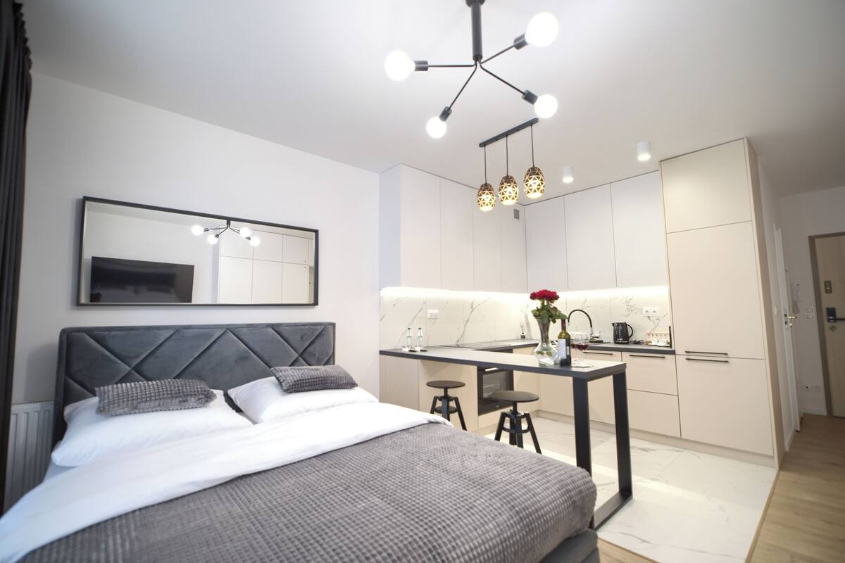Ein modernes Hotelzimmer mit einem Bett, einem Spiegel, einer Küchenzeile und einem Esstisch.