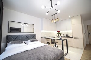 Una habitación de hotel moderna con cama, espejo, zona de cocina y mesa de comedor.