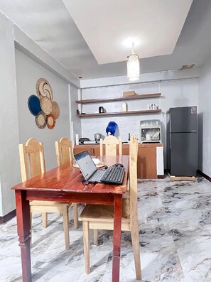 Un coin repas avec une table en bois, des chaises, un ordinateur portable et une cuisine en arrière-plan.