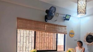 Ein Zimmer mit Holztisch und -stühlen, einem Ventilator, einem Fenster mit Holzjalousien und einer wandmontierten Lampe.