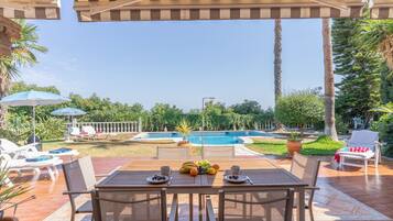 Eine Terrasse mit Tisch für Zwei, einem Pool und Liegestühlen.