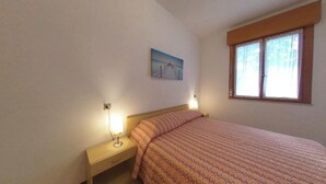 Una camera da letto con un letto, lampade sui comodini, un comodino, una finestra con tende e un quadro appeso al muro.