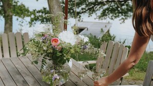 Una mesa de madera al aire libre con un centro de flores, copas de vino y una tabla de quesos.