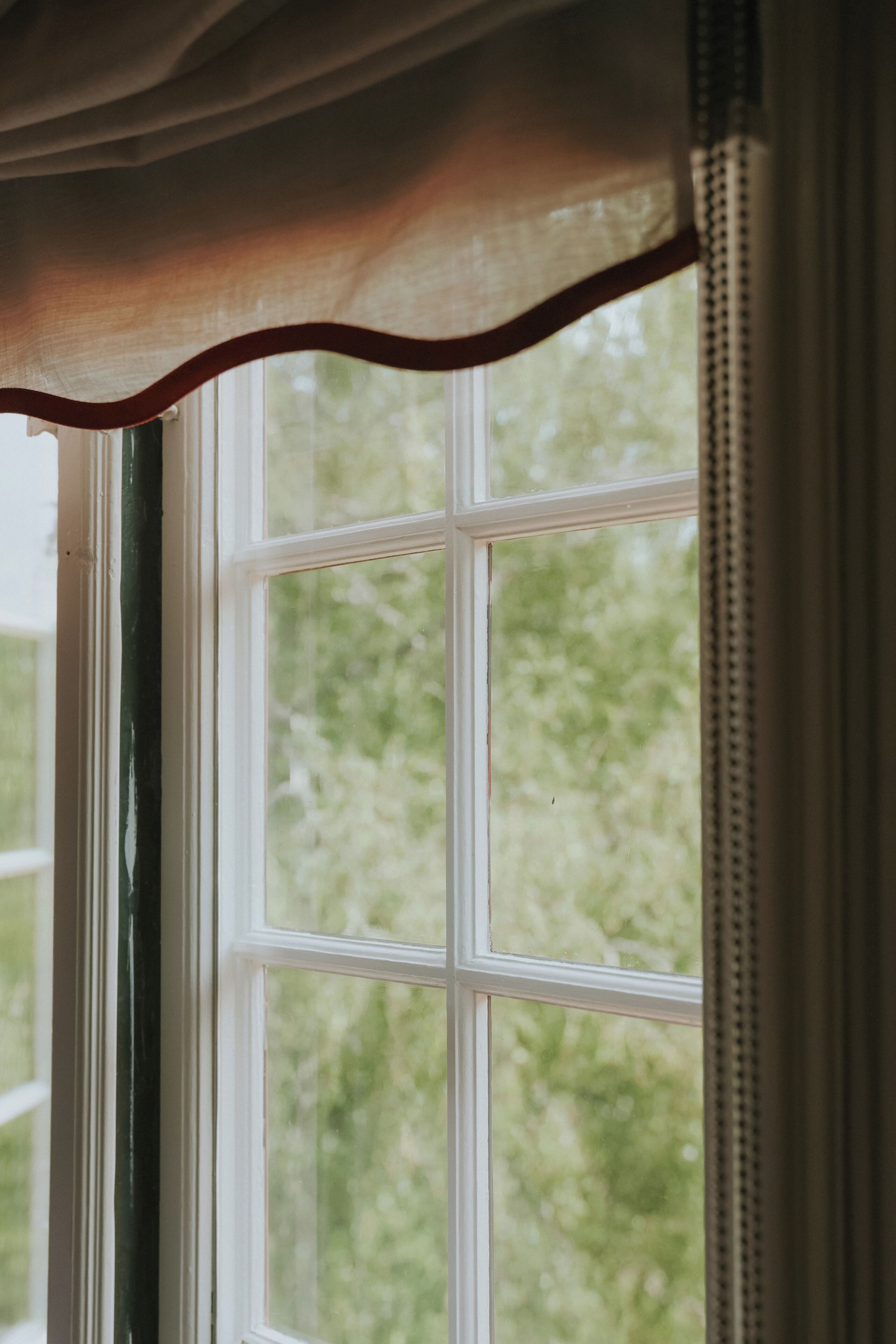 A window with a white frame and a greenish curtain.