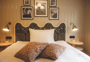 A bed with a decorative headboard, two bedside lamps, and framed pictures on the wall. - Badhotellet Villa Berg  (Norrtalje)