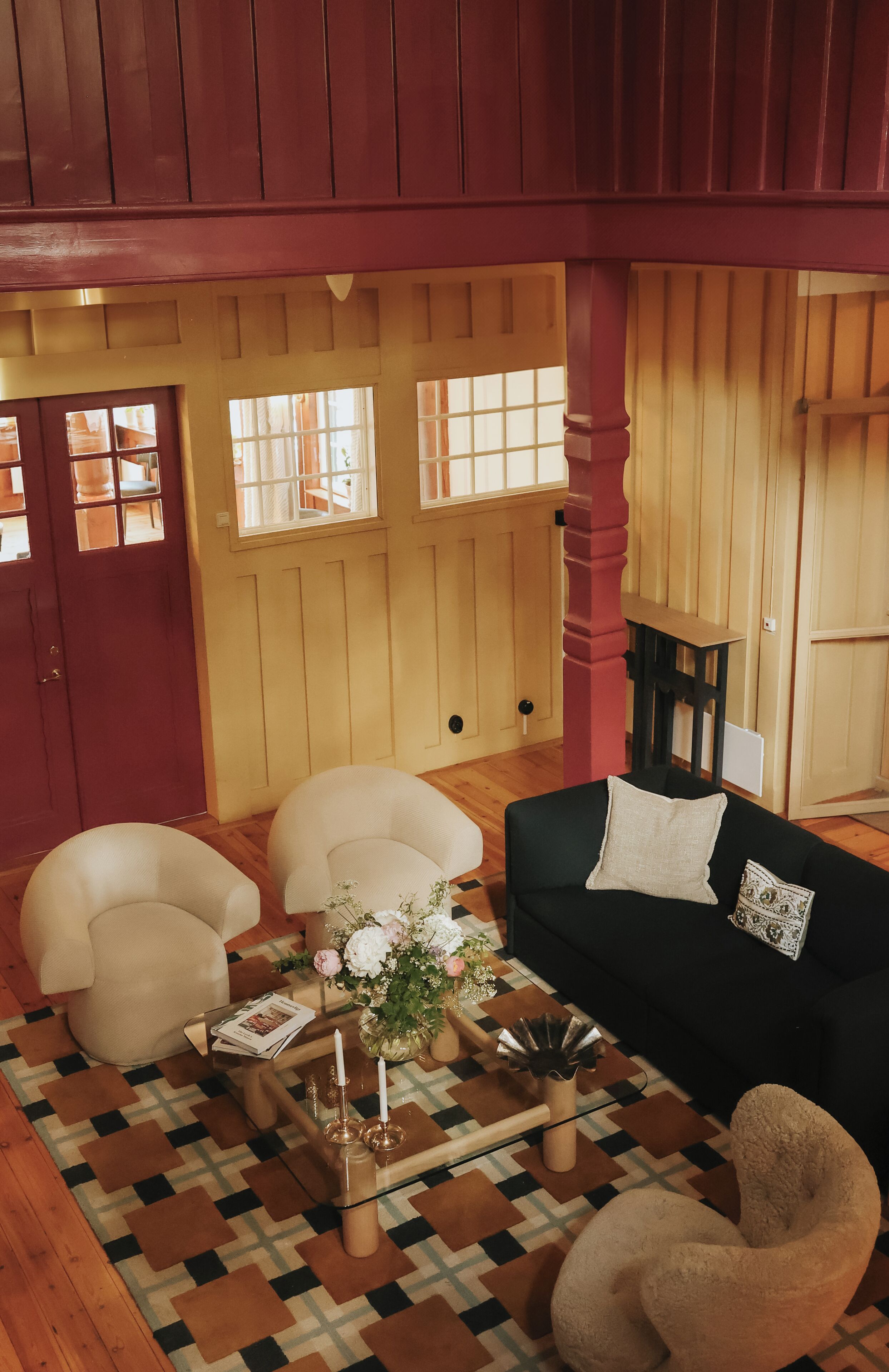 Een gezellige woonkamer met een zwarte bank, beige fauteuils, een glazen salontafel en een kamerkleed met dessin.