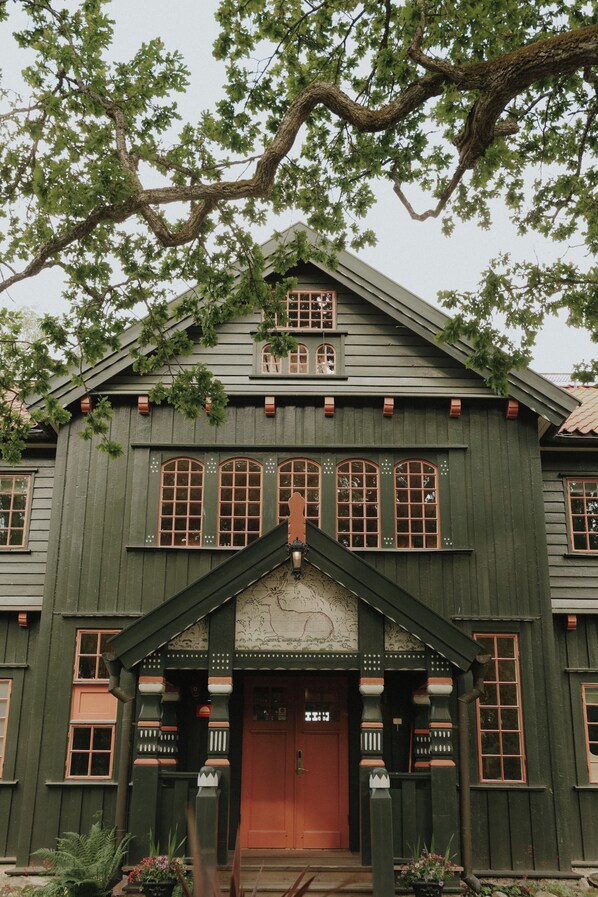 A large, two-story building with a steeply pitched roof, multiple windows with decorative trim, and a prominent front entrance with a red door. - Badhotellet Villa Berg (Norrtalje)