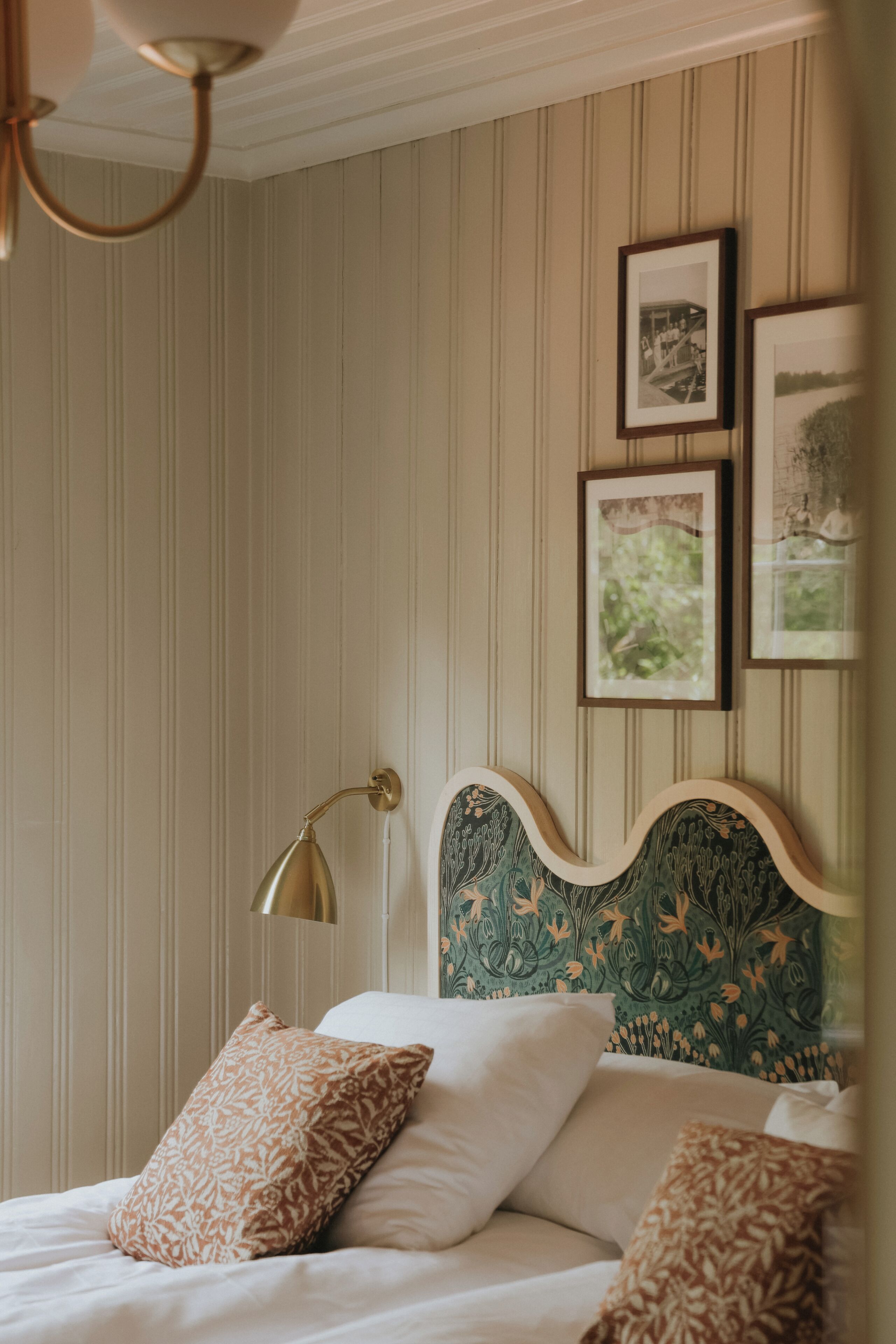 Une chambre avec un papier peint à rayures, un lit agrémenté d’oreillers à motifs, une tête de lit ornée de motifs floraux et deux tableaux encadrés accrochés au mur.