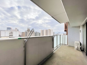 A balcony with a view of city buildings, a metal railing, and a tiled wall. - CITYSPIRE Namba Grace (Osaka)
