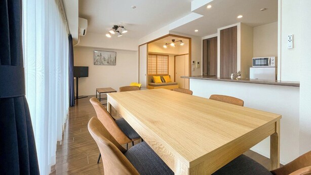 Ein modernes Wohnzimmer mit Holztisch, Sofas und einer Küchenzeile inklusive Mikrowelle.