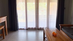 Quarto com mesa de madeira, um banco e vista através de portas deslizantes.