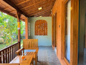 Un balcón de madera con una mesa y sillas, un panel de madera decorativo y vista a zonas verdes.