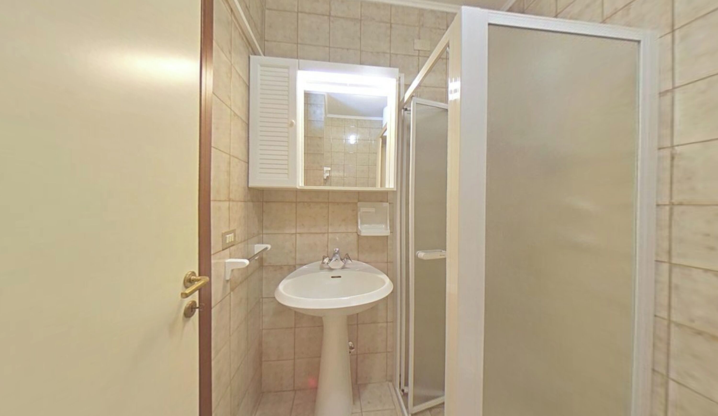 A bathroom with a sink, mirror, and shower enclosure.