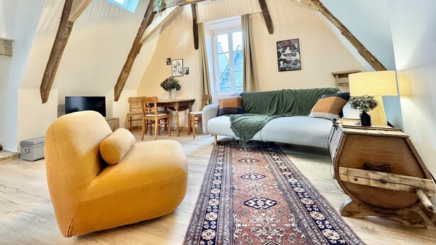 Un cuarto estilo loft con vigas de madera expuestas, un sofá, una silla, una mesa con sillas y un tapete estampado.