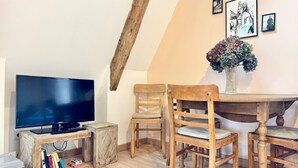 Una habitación acogedora con televisión, sillas de madera, una mesita y una estantería.