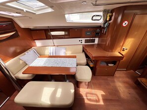 A compact interior with a sofa, a small table, a bench, a kitchenette, and a storage cabinet. - Sun-Kissed Sailing Adventure in Islas Sarónicas (Alimos)