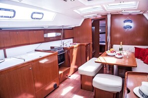 A compact galley with a sink, stove, and dining area with a table and chairs. - Sun-Kissed Sailing Adventure in Islas Sarónicas (Alimos)
