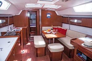 A yacht interior with a dining area, a bench, a small table with a bottle and glasses, and a sign on the wall. - Sun-Kissed Sailing Adventure in Islas Sarónicas (Alimos)