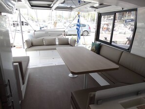 A compact interior with a sofa, a table, and a window overlooking a marina. - Sun-Kissed Sailing Adventure in Islas Sarónicas (Alimos)