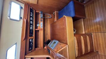 A compact interior with a wooden dashboard, a control panel, a blue cushioned seat, and a window.
