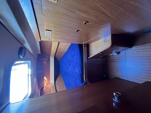 Un interior pequeño con ventana, una mesita y un cojín azul.