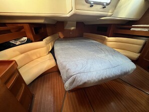A compact boat interior with a foldable bed, wooden cabinetry, and a small seating area.