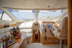 A boat interior with a steering wheel, control panel, cushioned seating, a beverage bucket, and a view of the outside. - Sun-Kissed Sailing Adventure in the Saronic Islands (Elliniko)