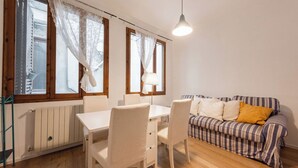 A room with a dining table, chairs, a striped sofa, and a hanging lamp. - Casa Gioia by MMega (Florence)