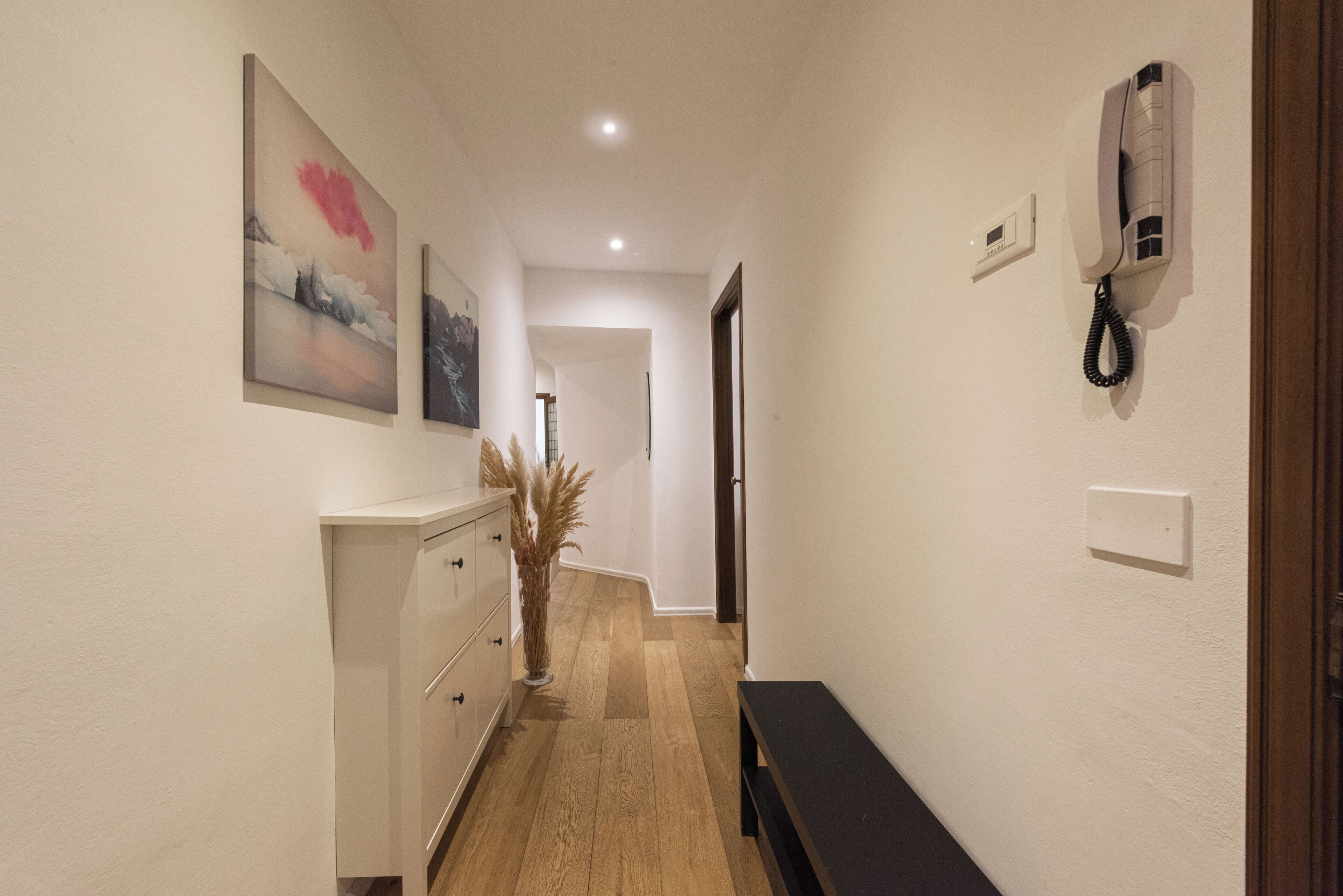 A hallway with a wooden floor, a white dresser, a bench, and a telephone on the wall.