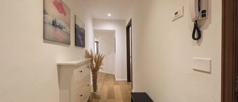 A hallway with a wooden floor, a white dresser, a bench, and a telephone on the wall.