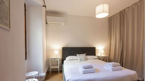 A bedroom with a large bed, two bedside tables, a wall-mounted air conditioner, and a ceiling light fixture. - Casa Gioia by MMega (Florence)