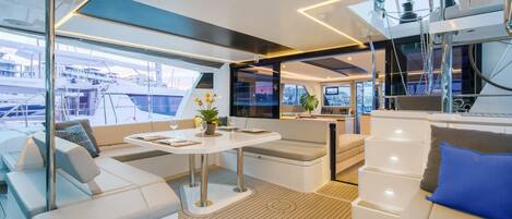 A modern yacht interior with a dining area, seating, and a view of the marina.