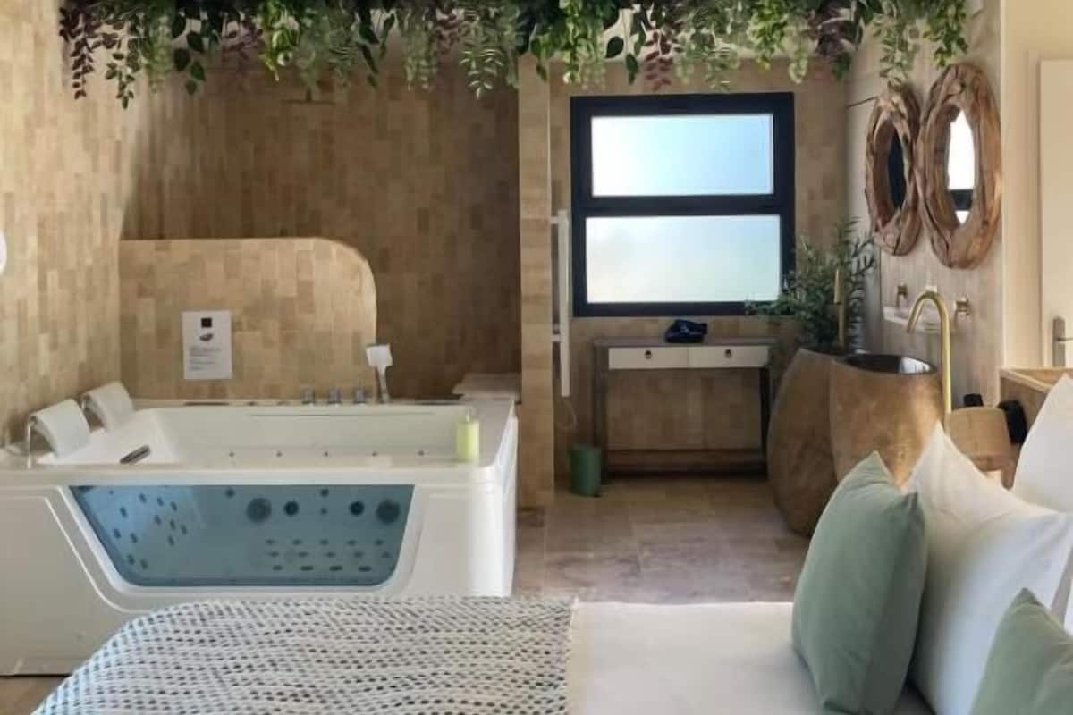 A room with a bathtub, a sofa with cushions, a mirror, and a wall-mounted TV.