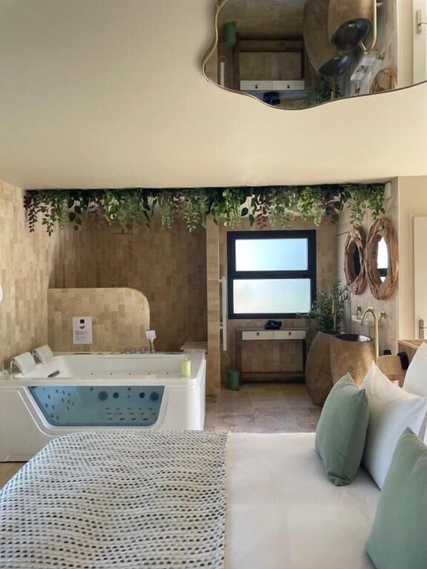 A room with a bathtub, a sofa with cushions, a mirror, and a wall-mounted TV.