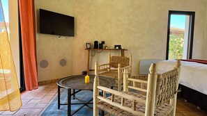 Habitació amb un llit, televisió penjada a la paret, taula petita amb una espelma i una cadira.