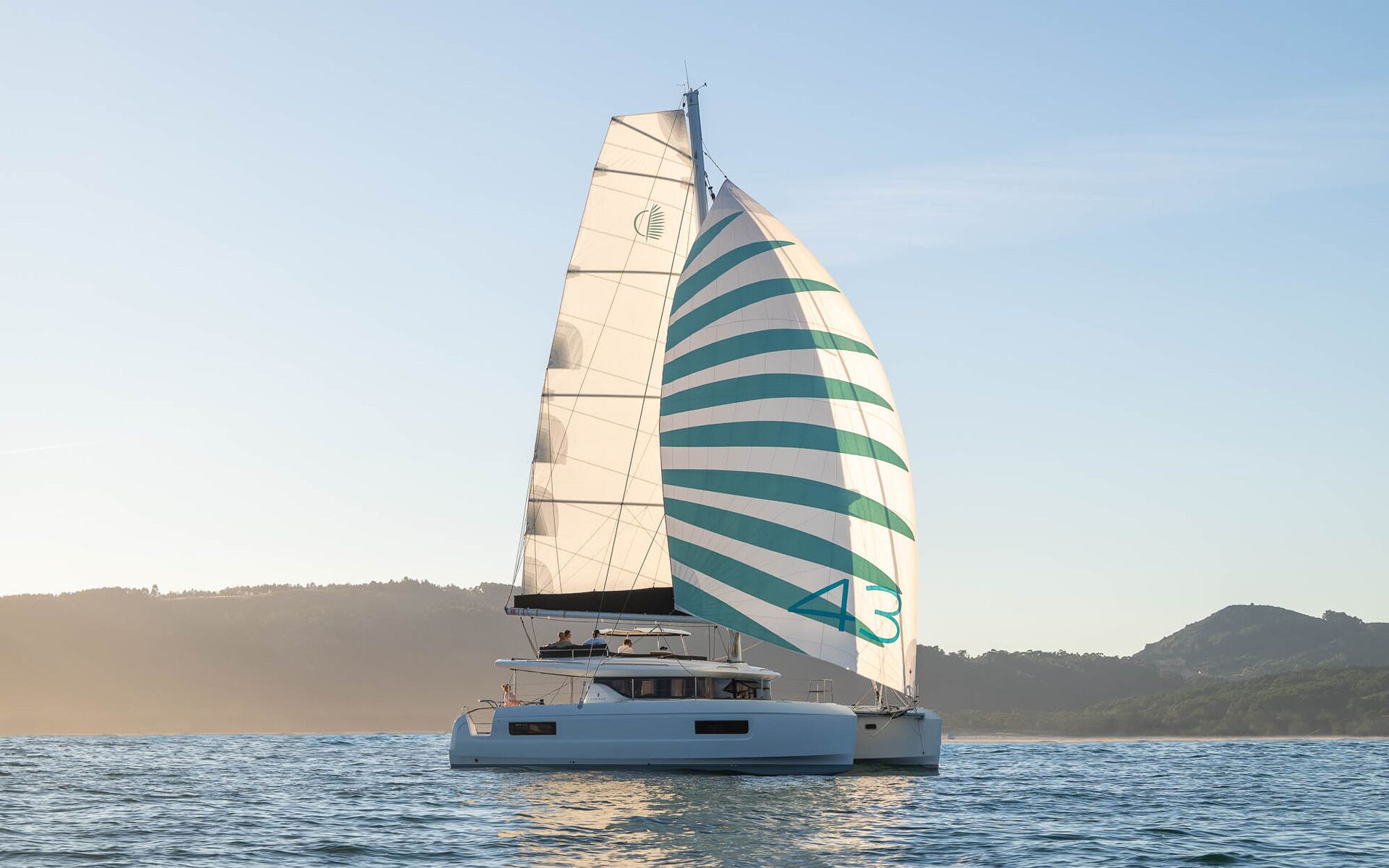 A sailboat with a striped sail, a cabin, and a view of the water and distant land.