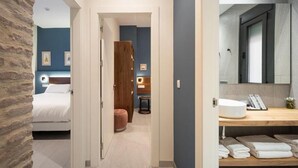 Hotellihuone, jossa on sänky, puinen vaatekaappi, pieni pöytä sekä kylpyhuone, jossa on pesuallas ja peili.