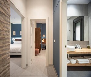 Een hotelkamer met een bed, een houten kledingkast, een kleine tafel en een badkamer met wastafel en spiegel.