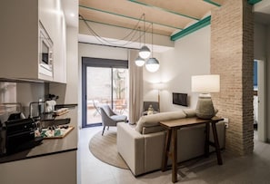 Een moderne hotelkamer met een kitchenette, een bank, een eettafel en een groot raam.